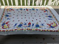 Full view of the vintage tablecloth showing the overall design with Dutch windmills, tulips, and figures in traditional clothing. The white background highlights the vibrant colors.