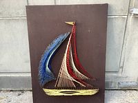 Front view of vintage string art sailboat on dark brown board, showing detailed string patterns in red, white, blue, and yellow threads.