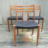 Front view showing three teak mid century modern dining chairs with black vinyl seats, one chair back design slightly different.