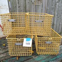 Photo showing the 4 yellow vintage coated wire locker baskets stacked in 2 rows outdoors, each with a metal label plate with IDs C 514, D 721, D 761, C 536.