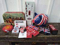 Photo showing all British-themed items assembled on wooden surface including Union Jack piggy bank, tins, bookmarks, ornaments, sticker, and boxing glove keychain.