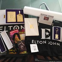 Full layout of all Elton John Farewell Yellow Brick Road tour items including keychain, luggage tag set, notebook, tote bag, VIP lanyard, tour book, shopping bag, pen/pencil set, and lithograph tube with certificate.