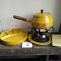 Full set showing yellow floral fondue pot with wooden handle on stand with burner, metal tray, and six yellow divided plates.