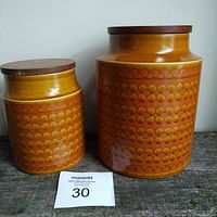 Two mid century modern Hornsea Saffron ceramic canisters side by side, wood lids, showing sizes and overall condition.