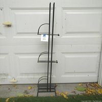 Full view of the tall black iron magazine stand with three horizontal shelves and curved side rails.