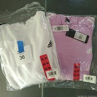 Two Adidas women's hoodies in original packaging, one white, one lilac, both size medium with tags