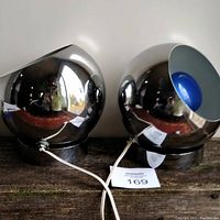 Pair of chrome spherical eyeball lamps side by side on wooden surface