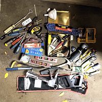 Overview of assorted hand tools and tool accessories laid out on concrete floor