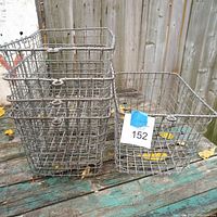 Five vintage wire locker baskets placed outdoors on a wooden surface, visible bent wires and rust spots on some baskets.