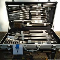 Full set of stainless steel BBQ utensils neatly arranged in an open metal case showing all items and the case handle.