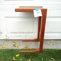 Side profile of the teak table showing the C-shaped design and wood grain.