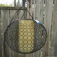 Full front view of large metal swag lamp hanging against wooden background showing spherical cage and inner fabric tube.