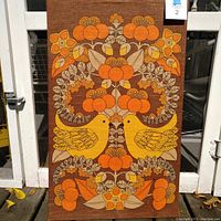 Full front view of the vintage stretched fabric art showing symmetrical design with two lovebirds and floral elements in orange, yellow, and brown.