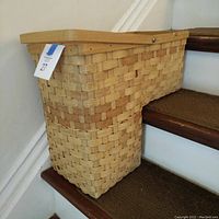 Side view of the woven stair basket showing shape and structure fitting over stair step with attached carry handle.