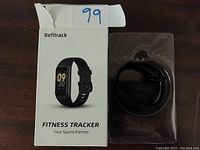 Photo showing Befitrack fitness tracker with black band in original white box with product image and branding.