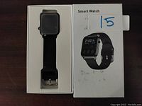 Smart watch displayed in open box on dark surface, watch face black and silicone band black.