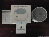 The Dreamegg white noise machine, its original box with product image, and instruction manual are shown. The device is round, white, with icons on top indicating power, light, fan, volume, and music functions.