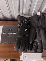 Pair of black heated gloves with battery pack and box labeled 'Heated Gloves HG10' by brand 4K on wooden surface