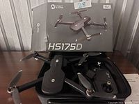 Holy Stone HS175D drone in carrying case with remote controller and original box behind them on a table.