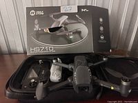 Holy Stone HS710 drone displayed with controller in open carrying case and the original box behind showing branding and product image.