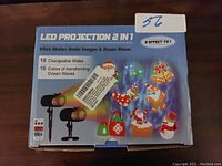 Box front showing 2 LED projectors with holiday-themed static images and ocean wave effects; labeled with features like 18 changeable slides and 10 color wave effects.