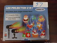 Front box image showing LED Projection 2 in 1 with holiday themed projections like Santa, snowman, and gifts. Details 18 changeable slides and 10 colors of transforming ocean waves.