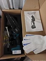 Boxed mini chainsaw with chain, user manual, white cotton gloves with blue grips, and small accessory components.