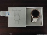Smart watch in white retail box showing watch face and band.