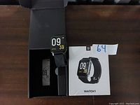 Smart Watch WATCH1 in black color, shown with its packaging box on a dark surface.