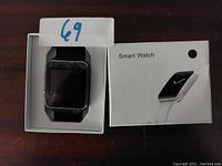 Smart watch with a black band placed inside its labeled white retail box.