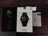 Soundpeats Watch 2 smart watch in black with display on, showing time 07:08, step count, date Mon 25, and calories burned 24.5. Included are the original white box with watch image and the user manual.
