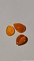 Three loose Fanta orange fire opal cabochons piled on a flat surface. Showcasing color and translucency.