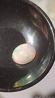 Oval cabochon Ethiopian opal with vibrant rainbow flashes on a black reflective surface, showing intense fire and play of color.