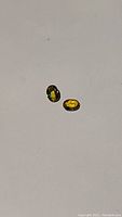 Pair of two oval sapphires, one multicoloured with blue and yellow hues, the other yellow, on a plain background.
