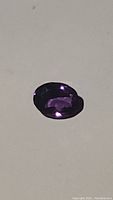Oval natural amethyst gemstone showing deep purple color in direct light.