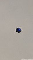 Photo showing the blue Ceylon sapphire on a neutral background with light reflection highlighting its polished cabochon surface.