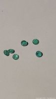 Six loose natural emerald gemstones displayed on a plain surface showing their green color and size.