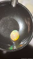 Close-up of oval cabochon cut Ethiopian opal with visible rainbow flashes on a dark holding surface.