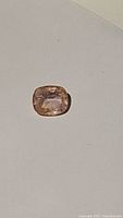 Close-up photo of the natural cushion cut pinkish yellow sapphire gemstone on a plain light background showing its color and cut.