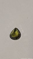 Teardrop-shaped green yellow sapphire gemstone showing color and cuts on white background.