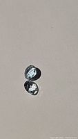Two natural soft blue aquamarine gemstones photographed on a neutral background, showing clarity and color.