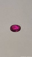 Oval cut natural treated ruby gemstone about 8.8x6.8mm showing hot pink purple color with clarity enhancements.