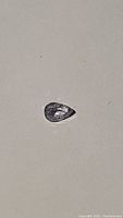 Close-up of a pear-shaped light blue-purple sapphire gemstone on a plain background, showing facets and clarity