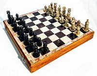 Chessboard set up with all pieces arranged for play, showing the marble squares and carved chess pieces in black and cream colors.
