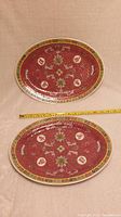 Photo showing two large oval Chinese Mun Shou Rose Longevity porcelain chargers laid flat with measuring tape to show size.