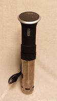 Full vertical view of Anova sous vide precision cooker showing stainless steel body and black handle with attached power cord.
