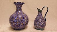 View of two antique Persian piriform-shaped metal vessels: a bulbous vase and a smaller jug, both intricately hand-painted with detailed geometric and floral patterns.