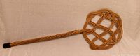 Full view of antique rattan rug beater showing woven circular head and handle with black cap.