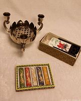 Mini metal candleholder with lotus flower design beside box of traditional Chinese solid ink sticks in various colors
