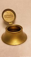 Brass Bradley Hubbard inkpot, lid open showing interior and embossed design on inside lid.